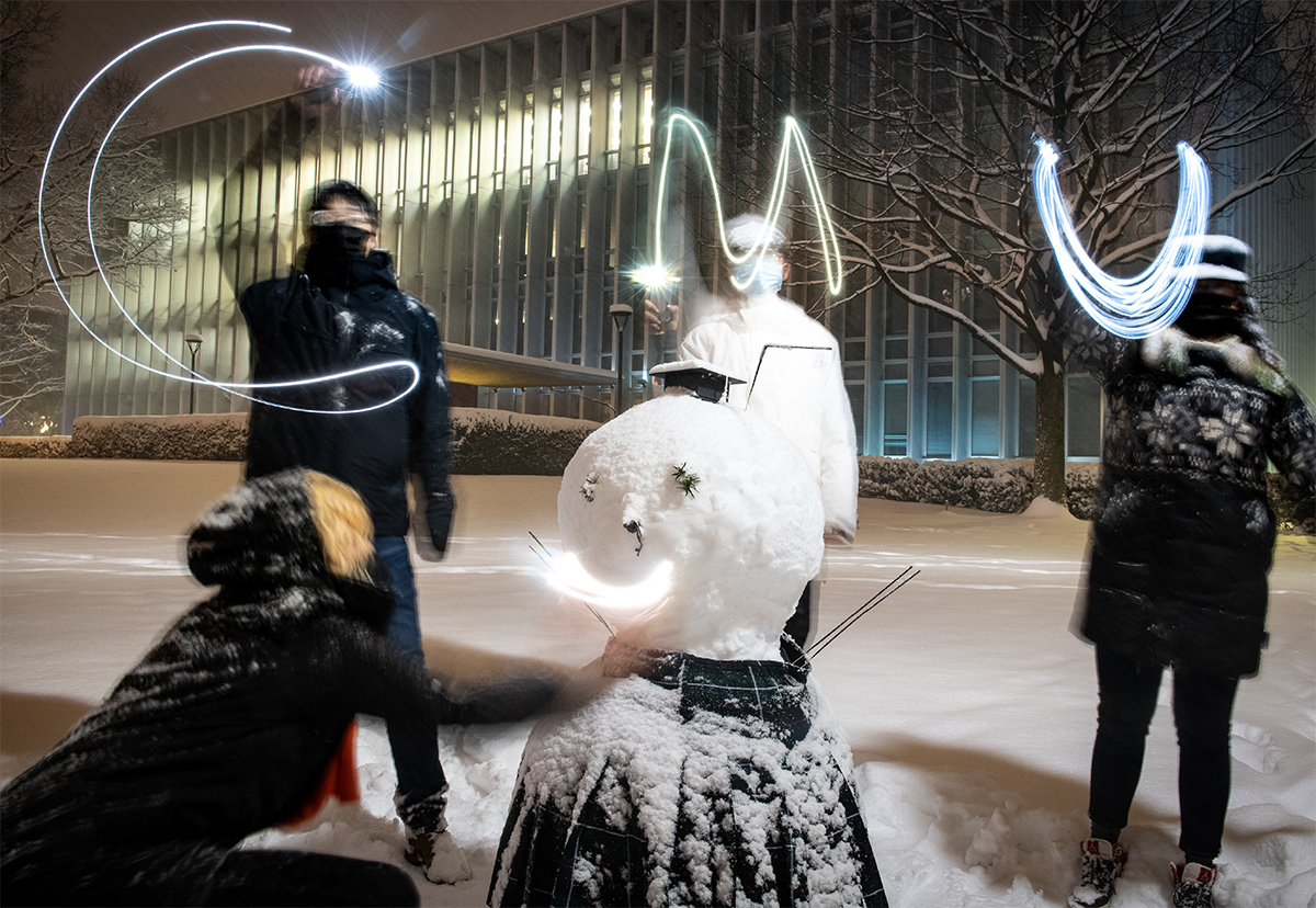 CMU staff and faculty build a snowman with CMU in lights in front of Hunt Library