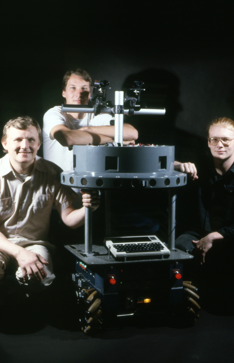 Hans Moravec, Mike Blackwell, and Jason Almeter pose with the Uranus robot, a project from the Mobile Robots Laboratory in the Robotics Institute. From the Robotics Institute Photograph Collection.