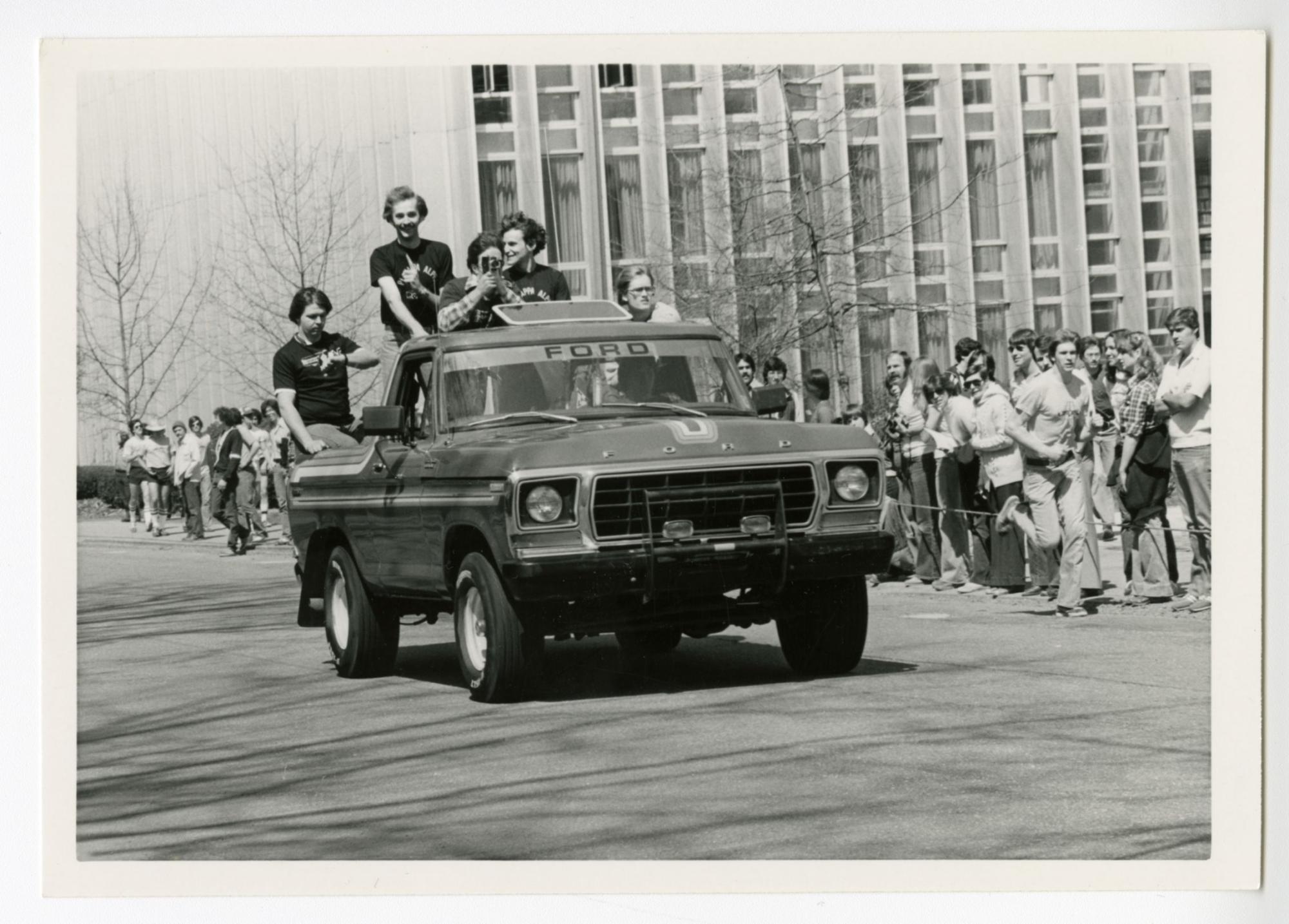 A 1970s model Ford F-100 truck drives down Frew Street as spectators watch from the sideline. Hunt Library can be seen in the background. (c.1975)