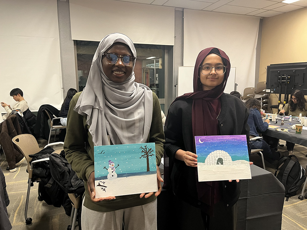 Attendees show off their paintings featuring a festive snowman and an igloo under a moon.