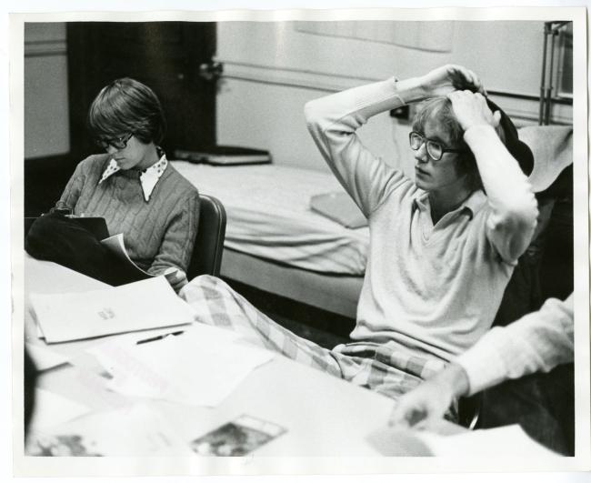 Two students sit at a conference table with papers and a folder on it. The back of the photograph is stamped with: "Photograph By Freeman."